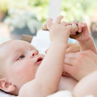 Eine Nahaufnahme des Gesichts und der Hände eines Babys, wobei der Schwerpunkt auf den Augen des Babys und der sanften Berührung durch die Hand eines Erwachsenen liegt.