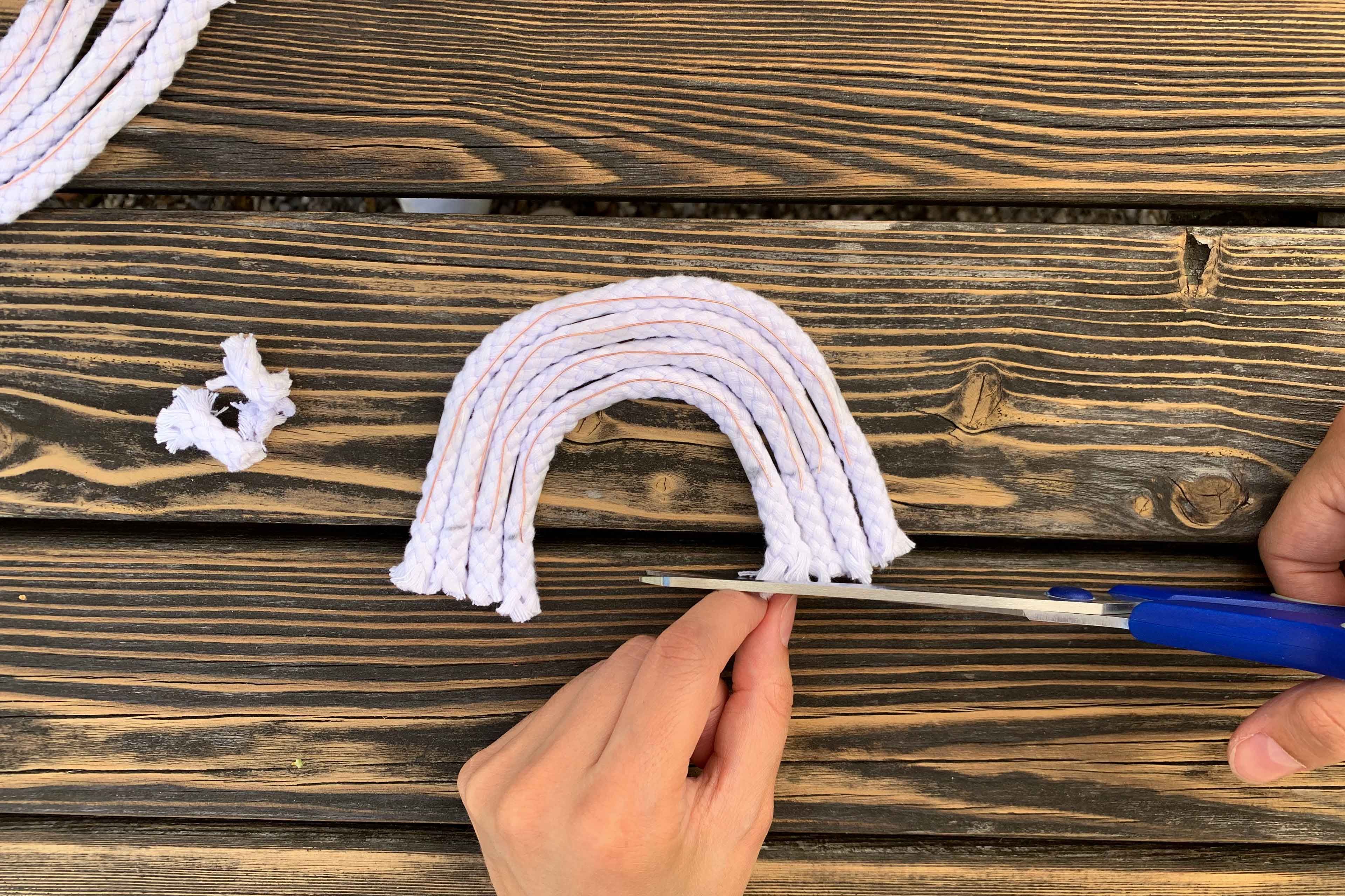 Eine Hand hält eine Schere und schneidet ein weißes, seilartiges Material in eine gebogene Form, die einem Regenbogen ähnelt.