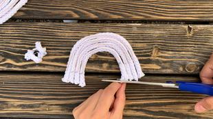 Eine Hand hält eine Schere und schneidet ein weißes, seilartiges Material in eine gebogene Form, die einem Regenbogen ähnelt.
