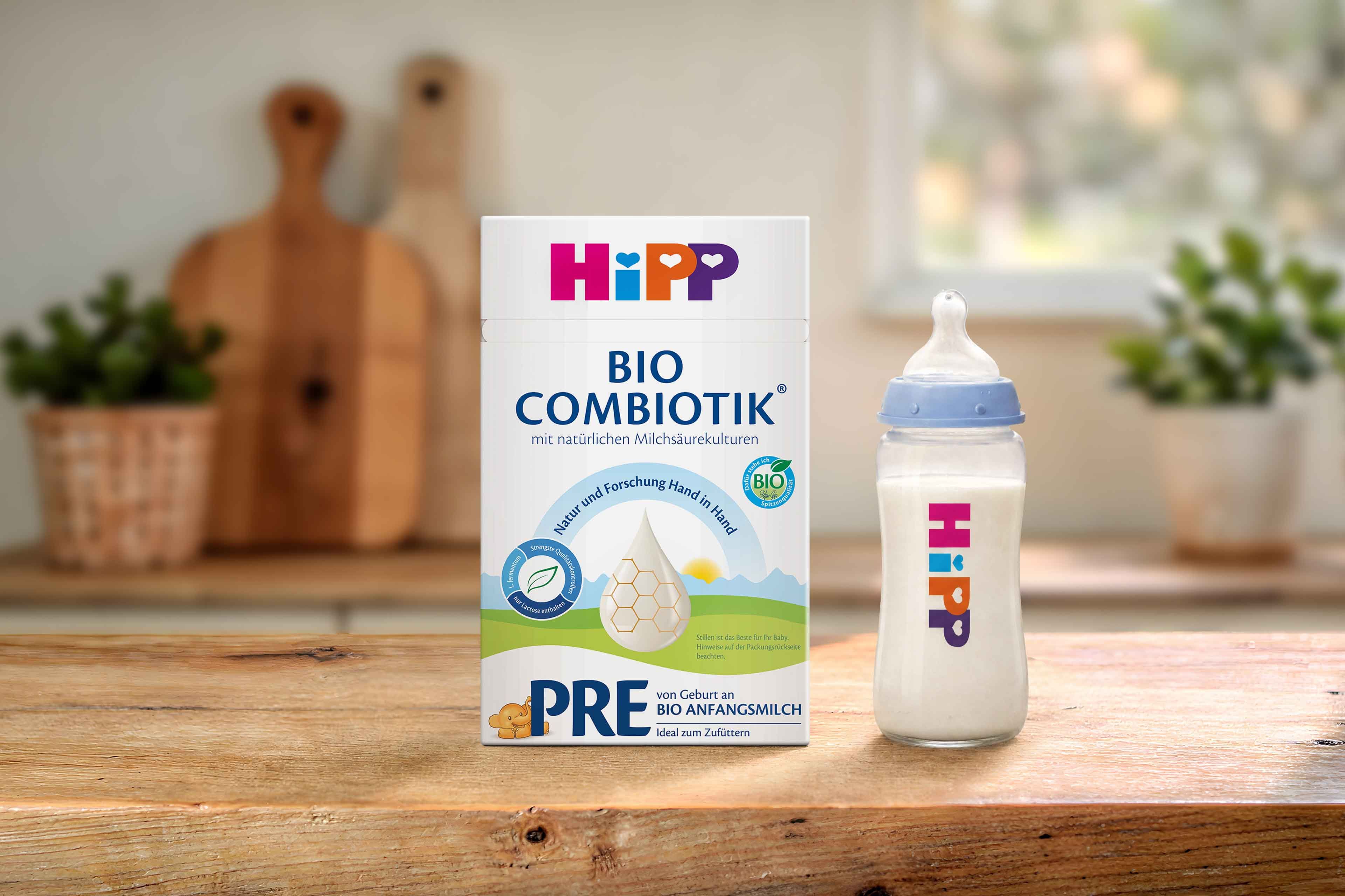 HiPP PRE BIO COMBIOTIK® Anfangsmilchpackung mit Bio-Siegel neben gefülltem Babyfläschchen auf Holztisch in heller Küche.