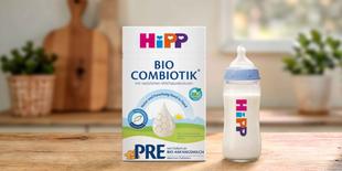 HiPP PRE BIO COMBIOTIK® Anfangsmilchpackung mit Bio-Siegel neben gefülltem Babyfläschchen auf Holztisch in heller Küche.