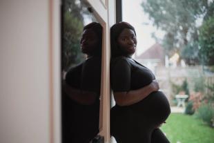 A pregnant woman holding her baby bump while standing against a wall outside