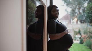 A pregnant woman holding her baby bump while standing against a wall outside