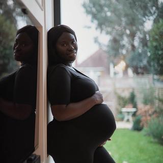 A pregnant woman holding her baby bump while standing against a wall outside