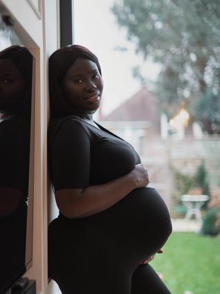 A pregnant woman holding her baby bump while standing against a wall outside