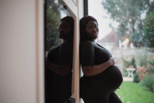 A pregnant woman holding her baby bump while standing against a wall outside