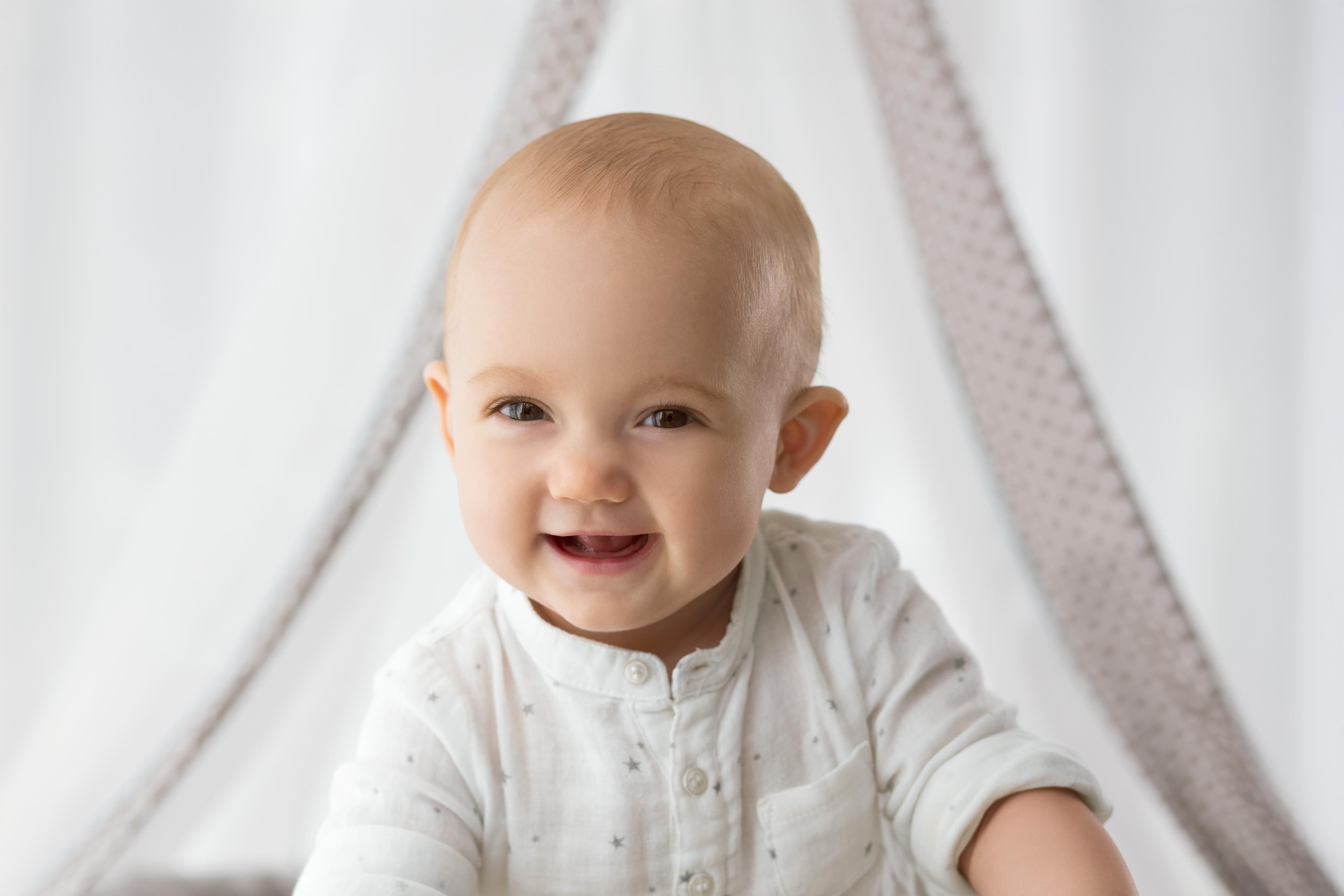 Baby sitzt vor einem weißen Hintergrund mit einem weißen Stoffzelt