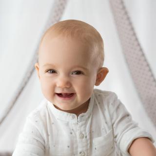 Baby sitzt vor einem weißen Hintergrund mit einem weißen Stoffzelt