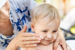 Eine Frau trägt Sonnenschutzmittel auf das Gesicht eines Babys auf.