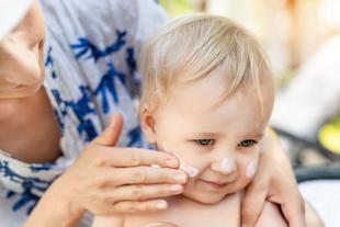 Eine Frau trägt Sonnenschutzmittel auf das Gesicht eines Babys auf.