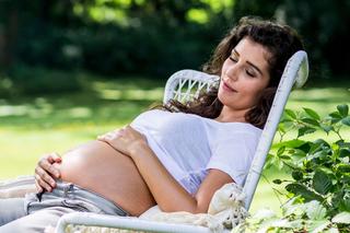 Entspannte schwangere Frau im Garten, die barfuß im Liegestuhl sitzt und liebevoll ihren Babybauch hält