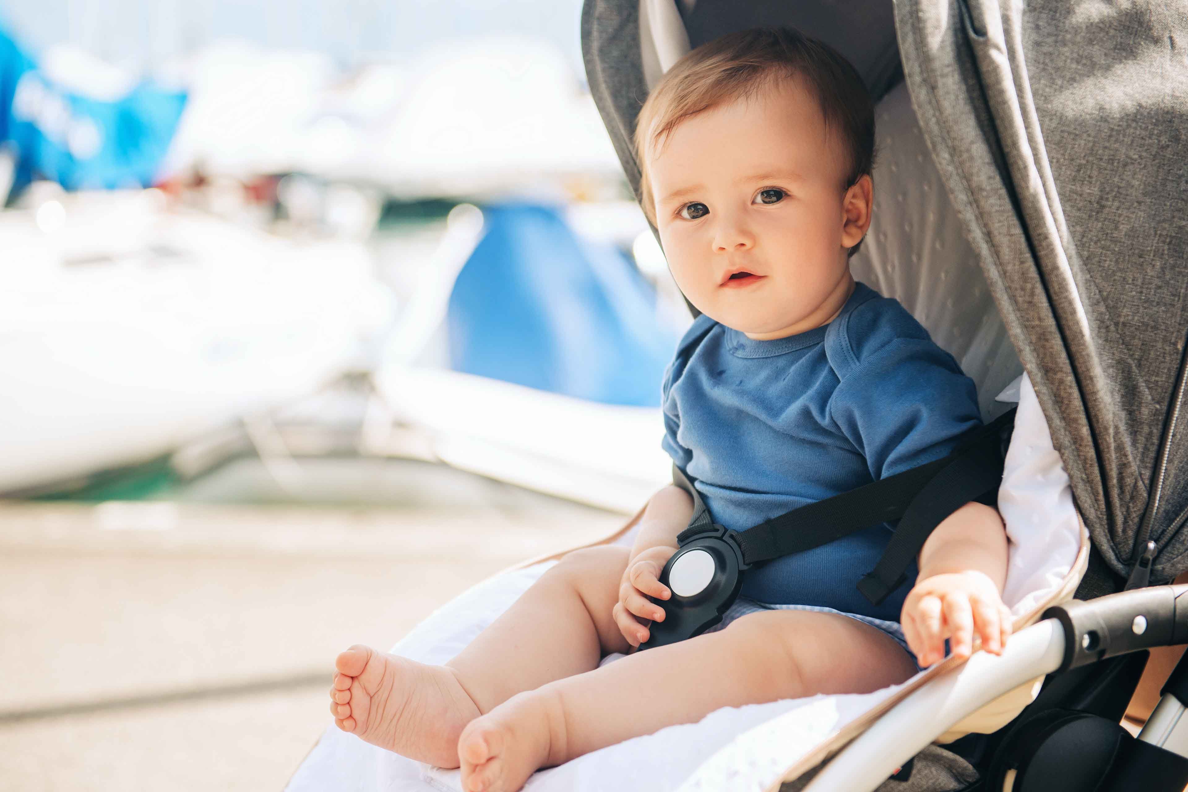 Ein Baby, das in einem Kinderwagen sitzt und mit konzentriertem Blick nach vorne schaut, vor einem Hintergrund aus Booten und Wasser.