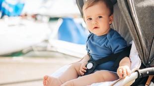Ein Baby, das in einem Kinderwagen sitzt und mit konzentriertem Blick nach vorne schaut, vor einem Hintergrund aus Booten und Wasser.