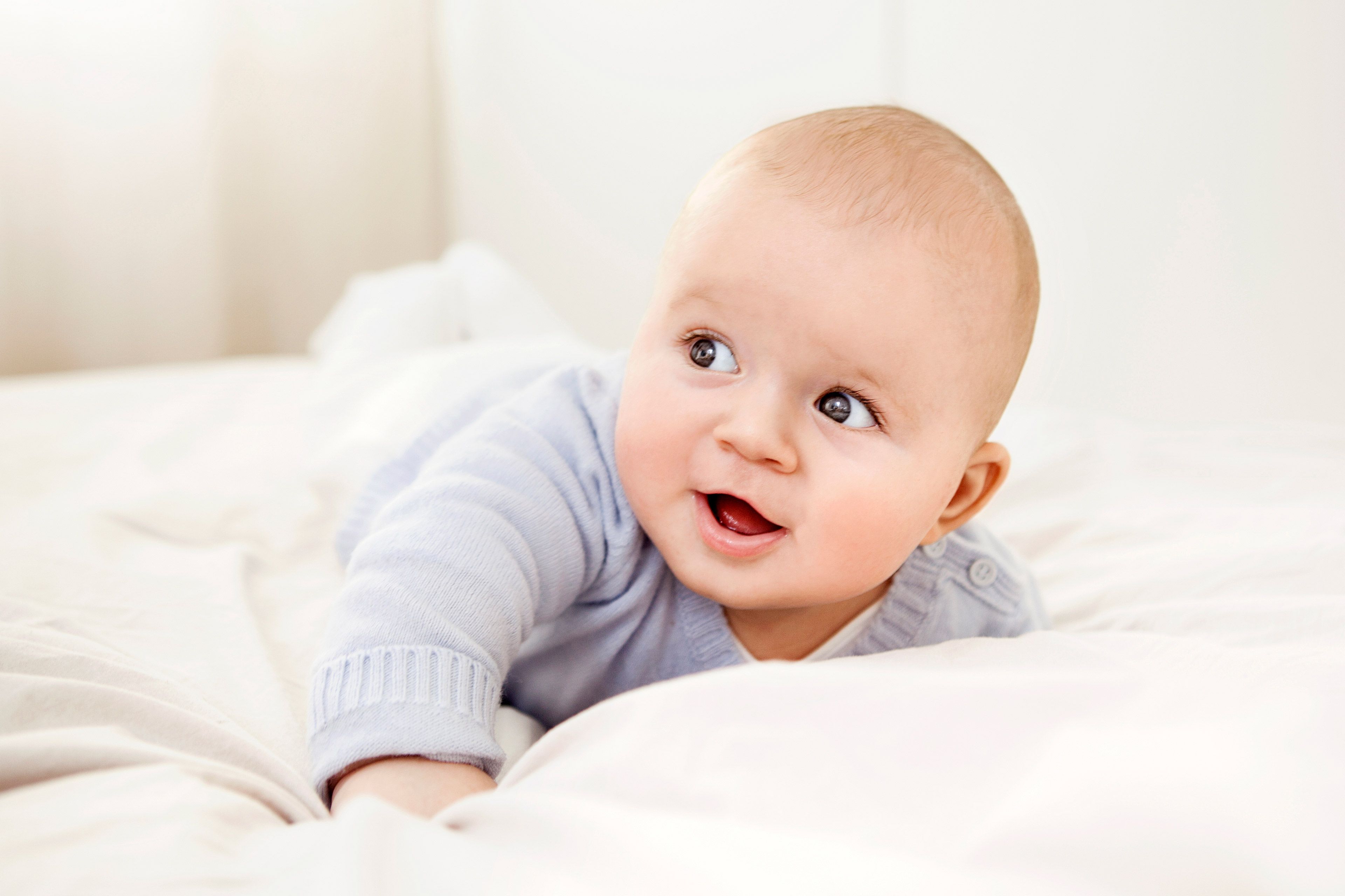 Baby liegt auf dem Bauch auf weißer Bettdecke in hellem Raum