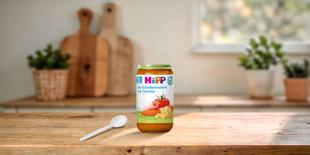 HiPP Bio-Schinkennudeln mit Gemüse 250g im Glas auf Holztisch, mit Löffel davor in heller Küchenumgebung