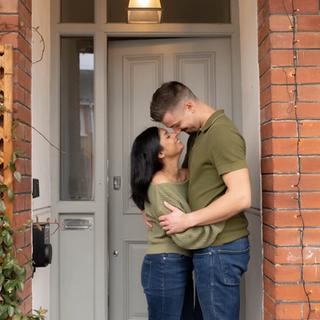 Couple embracing and smiling lovingly at each other while standing in front of their decorated home entrance.
