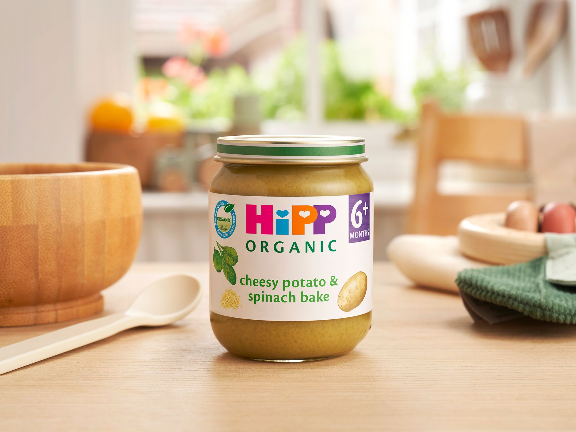 HiPP Organic Cheesy Potato & Spinach Bake on a dining table next to a bowl and spoon