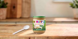 HiPP Bio-Gläschen Banane Kokosmilch in Apfel mit Hafer ab 6. Monat auf Holztisch mit Löffel in heller Küche