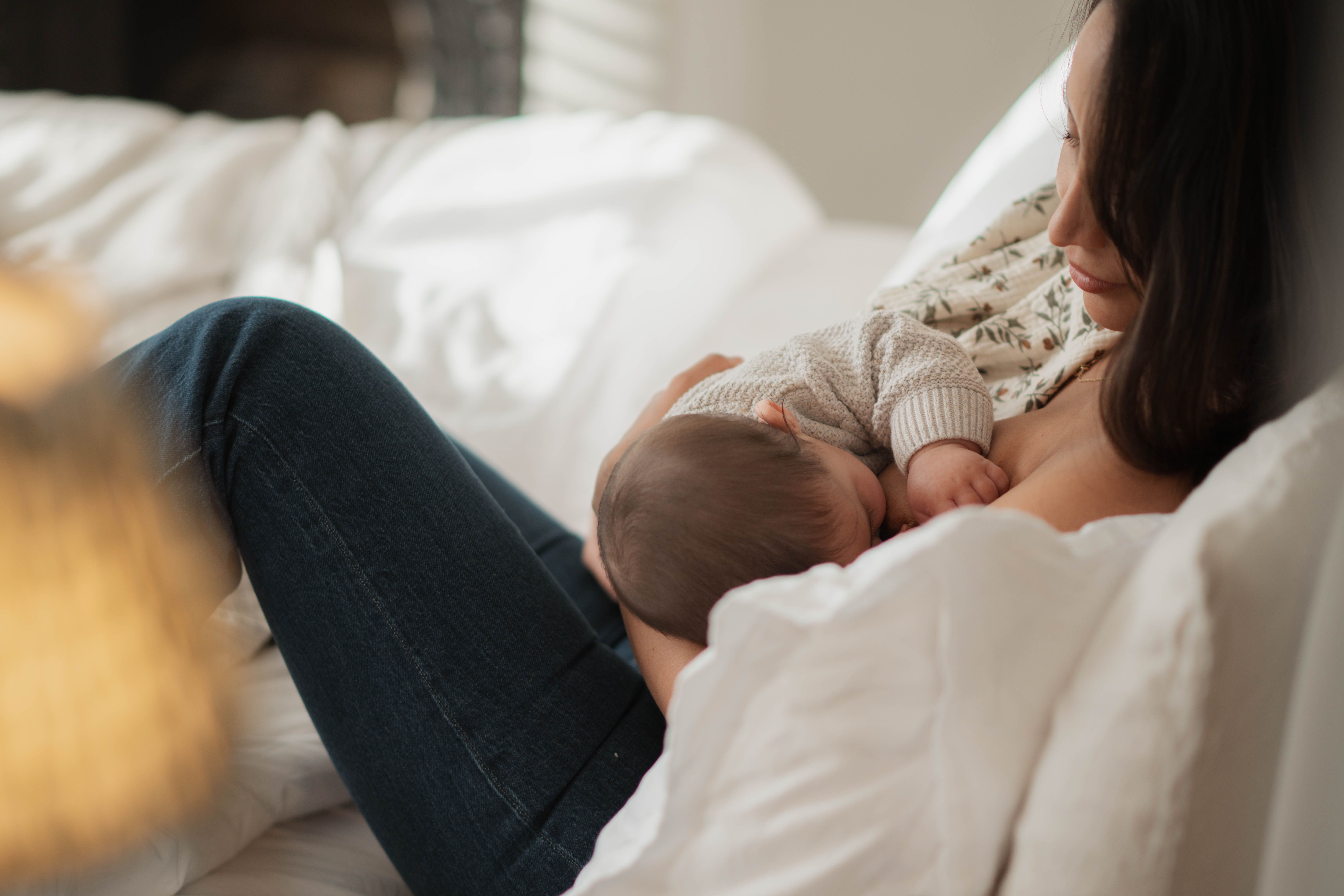 Mother breastfeeding her baby while relaxing on a bed, showing calm, close skin-to-skin bonding in the postpartum period