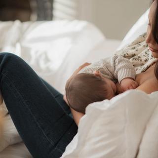 Mother breastfeeding her baby while relaxing on a bed, showing calm, close skin-to-skin bonding in the postpartum period