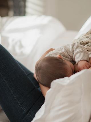 Mother breastfeeding her baby while relaxing on a bed, showing calm, close skin-to-skin bonding in the postpartum period