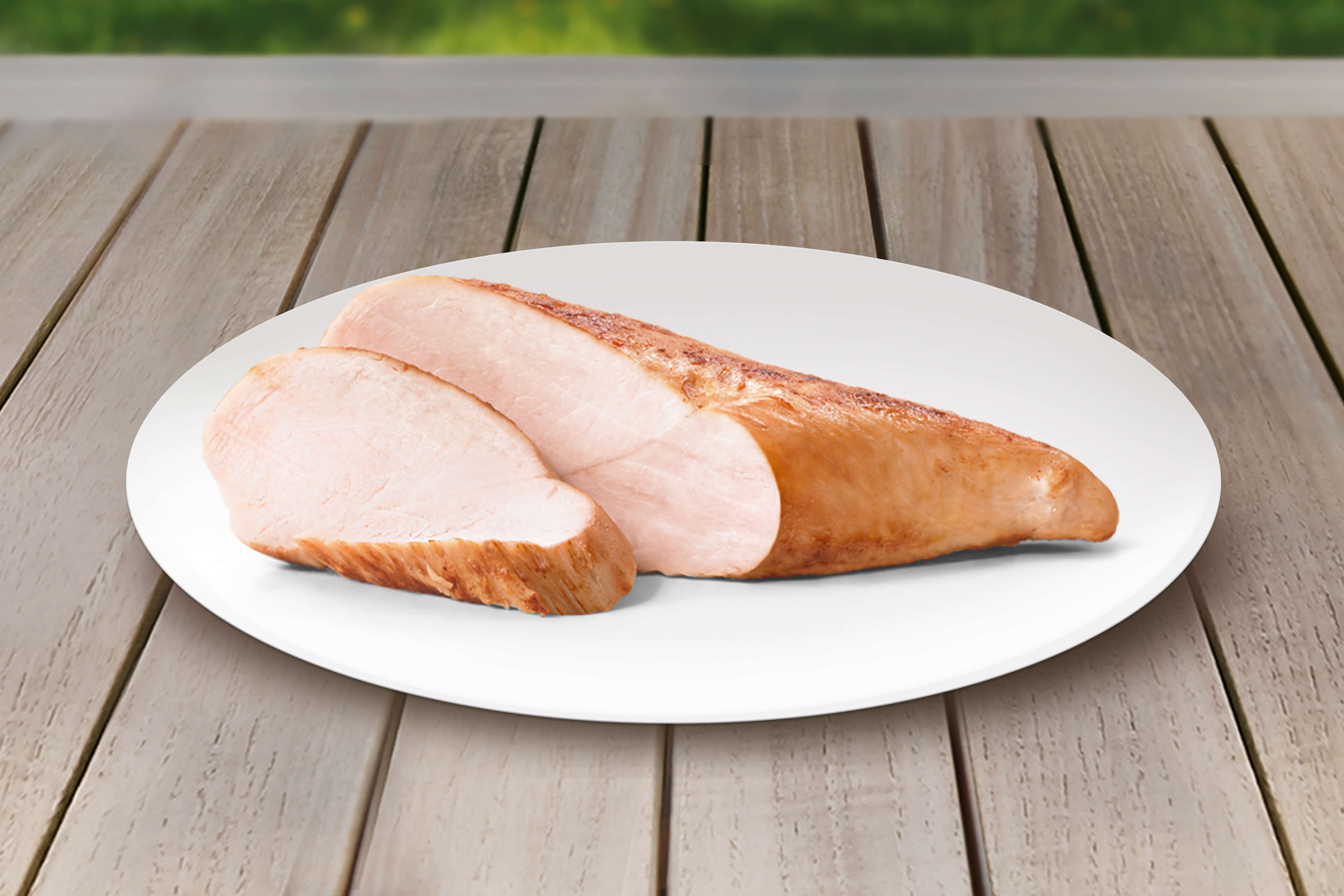 Ein in Scheiben geschnittenes Stück Fleisch, vermutlich Truthahn, auf einem weißen Teller vor einem hölzernen Hintergrund.
