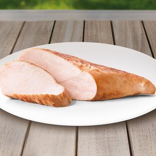 Ein in Scheiben geschnittenes Stück Fleisch, vermutlich Truthahn, auf einem weißen Teller vor einem hölzernen Hintergrund.