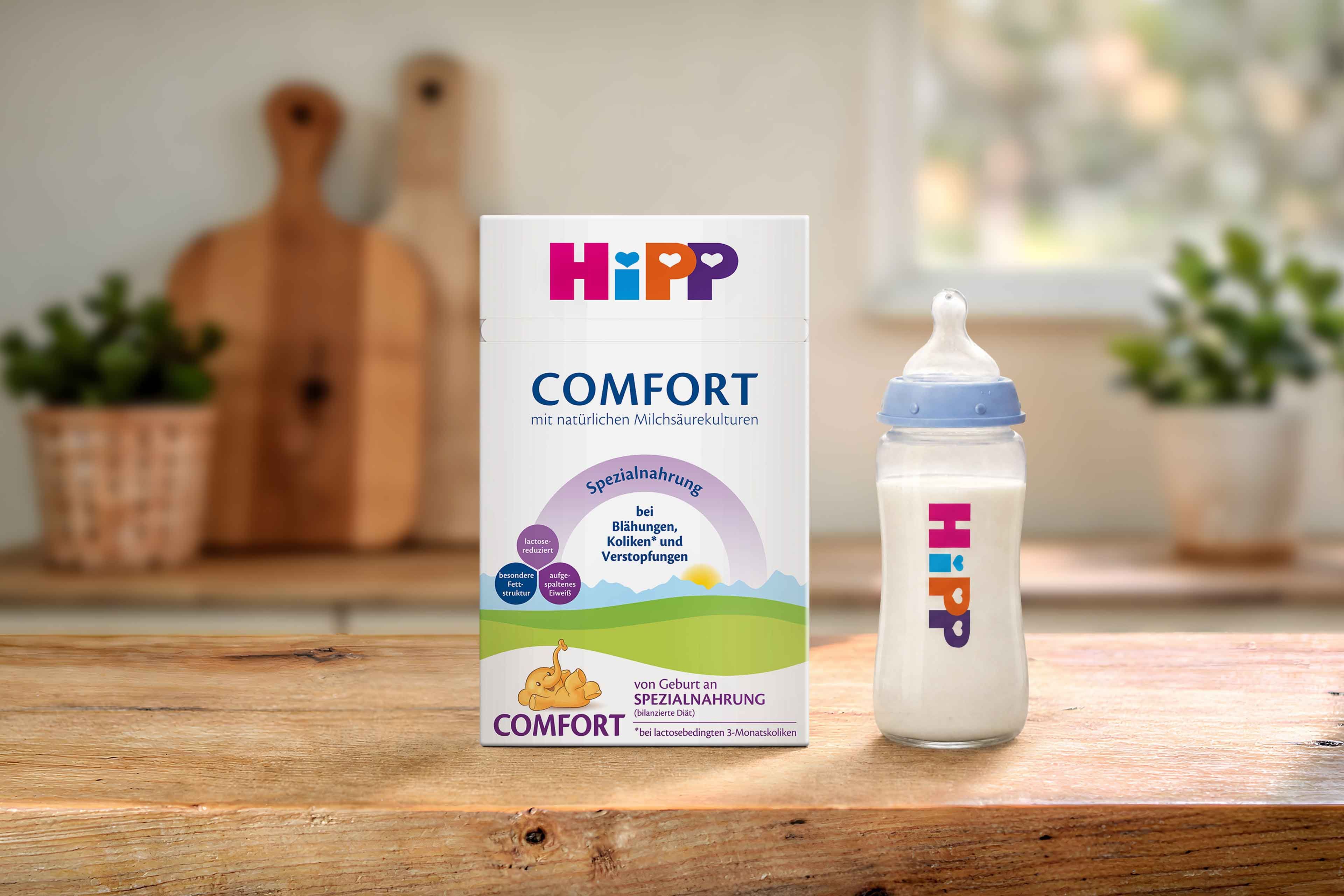 HiPP Comfort Spezialnahrung Packung und gefülltes Babyfläschchen auf Holztisch in heller, gemütlicher Küche