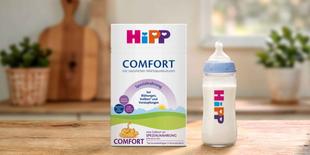 HiPP Comfort Spezialnahrung Packung und gefülltes Babyfläschchen auf Holztisch in heller, gemütlicher Küche