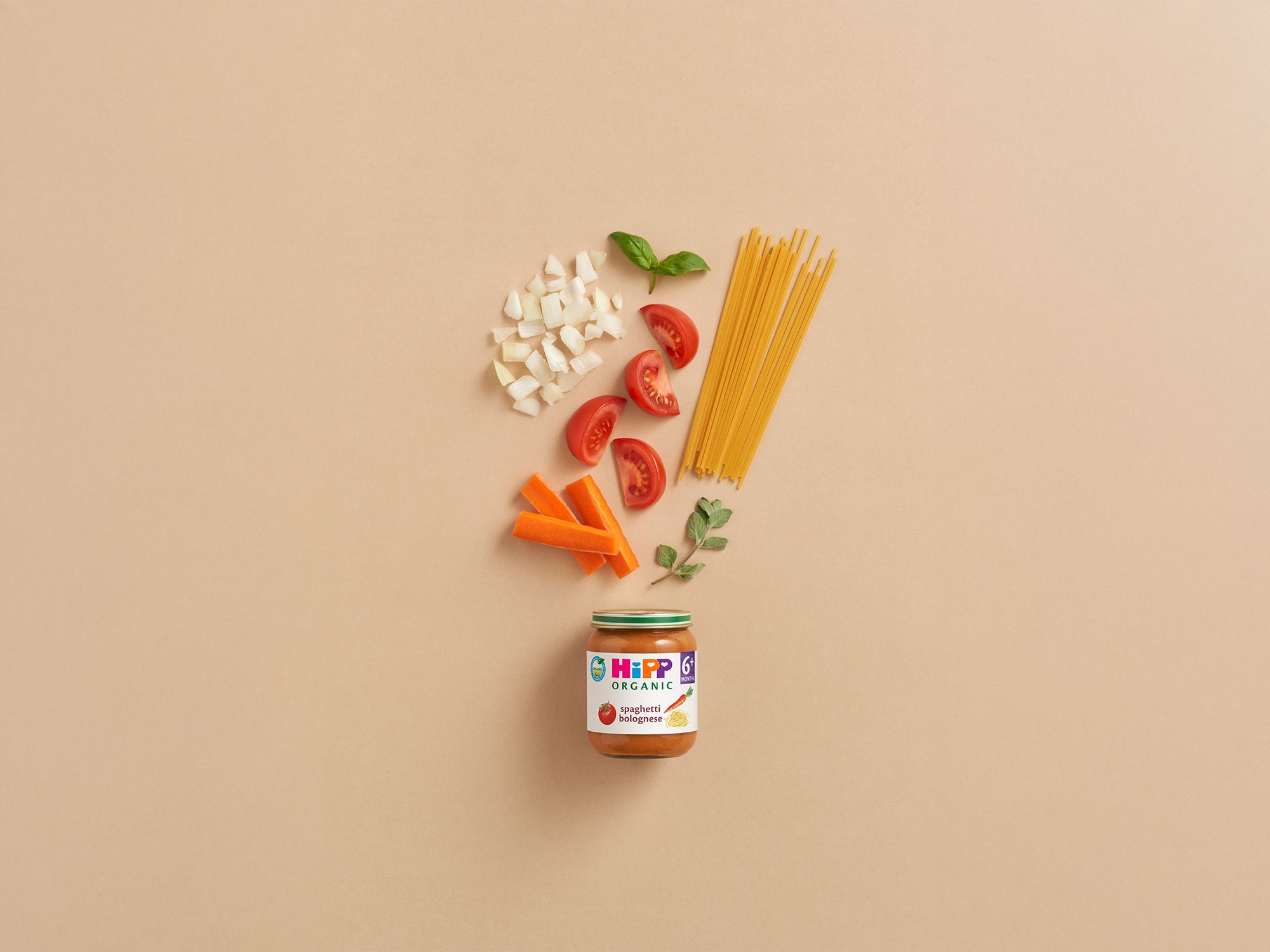 HiPP Organic Spaghetti Bolognese 6+ months jar with raw pasta, tomatoes, carrots, onions and herbs on a neutral background