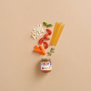 HiPP Organic Spaghetti Bolognese 6+ months jar with raw pasta, tomatoes, carrots, onions and herbs on a neutral background