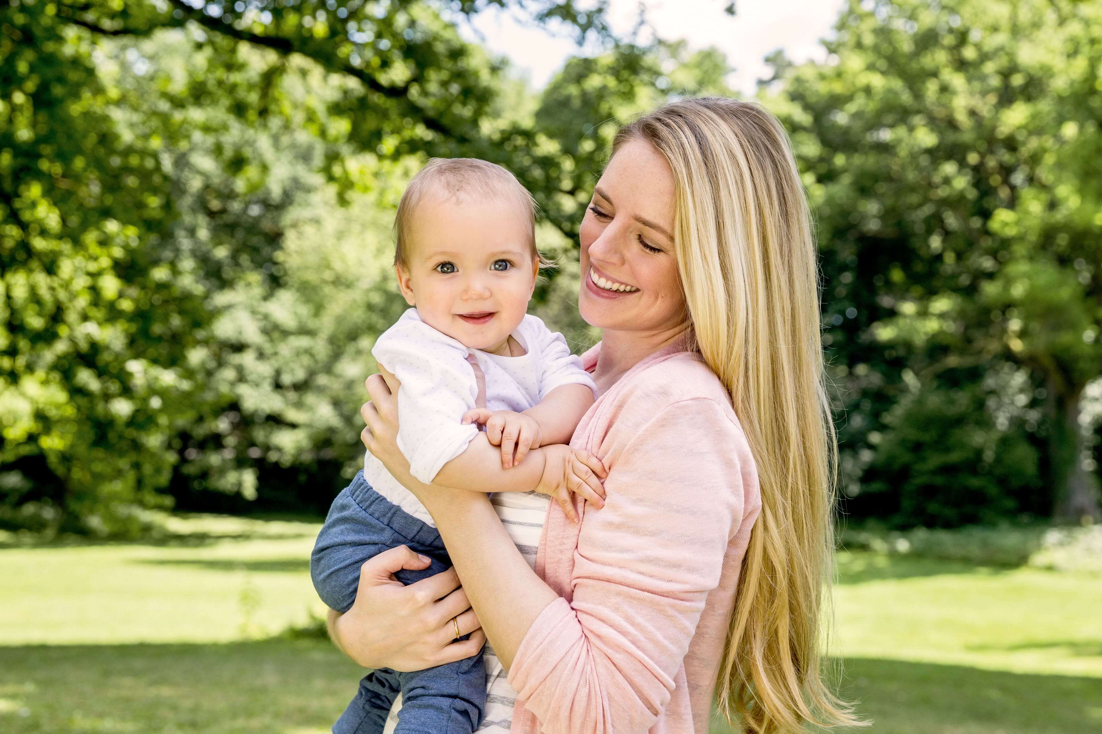 Ein freudiger Moment zwischen einer Mutter und ihrem Baby vor einer grünen Kulisse.