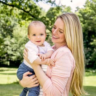 Ein freudiger Moment zwischen einer Mutter und ihrem Baby vor einer grünen Kulisse.