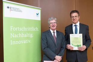 Johannes Doms erhält in Berlin eine EMAS-Urkunde zum Umweltmanagement 2016 von Dr. Ulrich Hatzfeld, beide im Anzug vor EMAS-Roll-up.