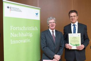 Johannes Doms erhält in Berlin eine EMAS-Urkunde zum Umweltmanagement 2016 von Dr. Ulrich Hatzfeld, beide im Anzug vor EMAS-Roll-up.