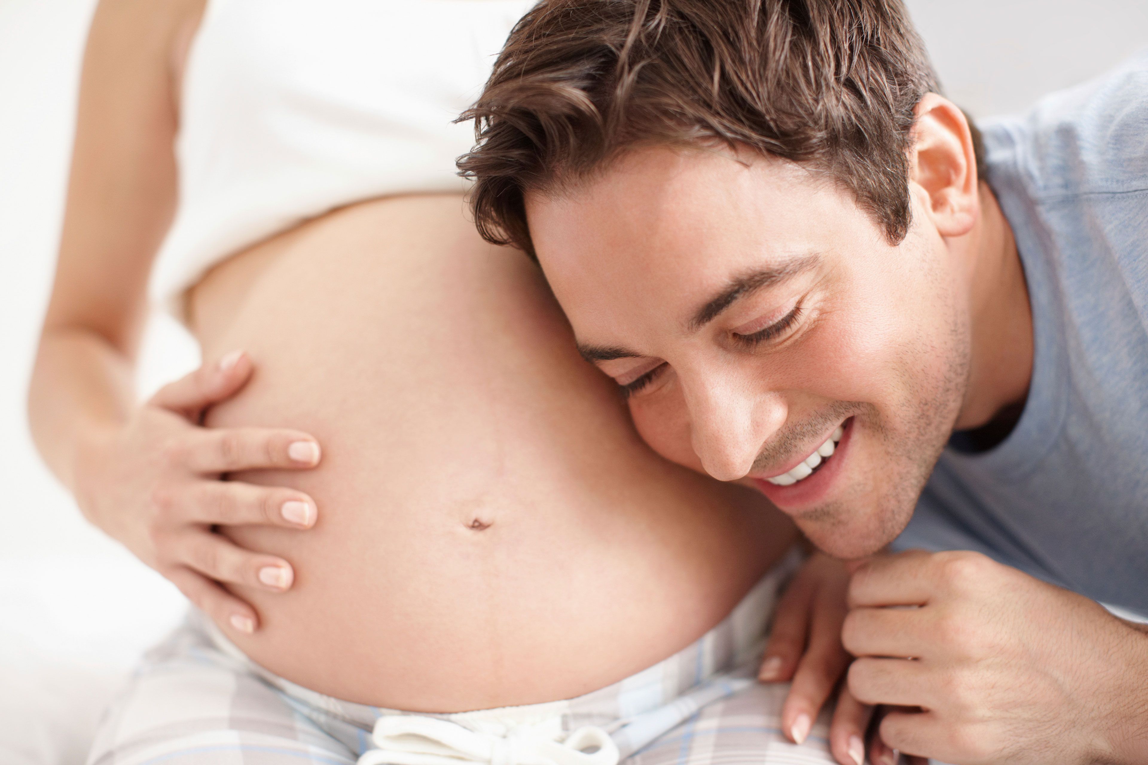 Ein Mann lauscht freudig den Geräuschen des Bauches einer schwangeren Frau.