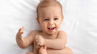 Ein Baby liegt auf einer weißen Fläche, lächelt und spielt mit seinen Füßen.