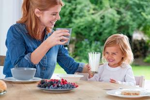 Mutter und Kleinkind frühstücken fröhlich zusammen, das Kind trinkt ein Glas Milch als Teil einer ausgewogenen Mahlzeit