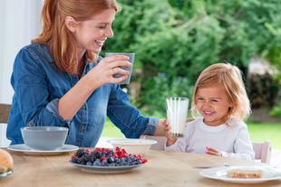 Mutter und Kleinkind frühstücken fröhlich zusammen, das Kind trinkt ein Glas Milch als Teil einer ausgewogenen Mahlzeit
