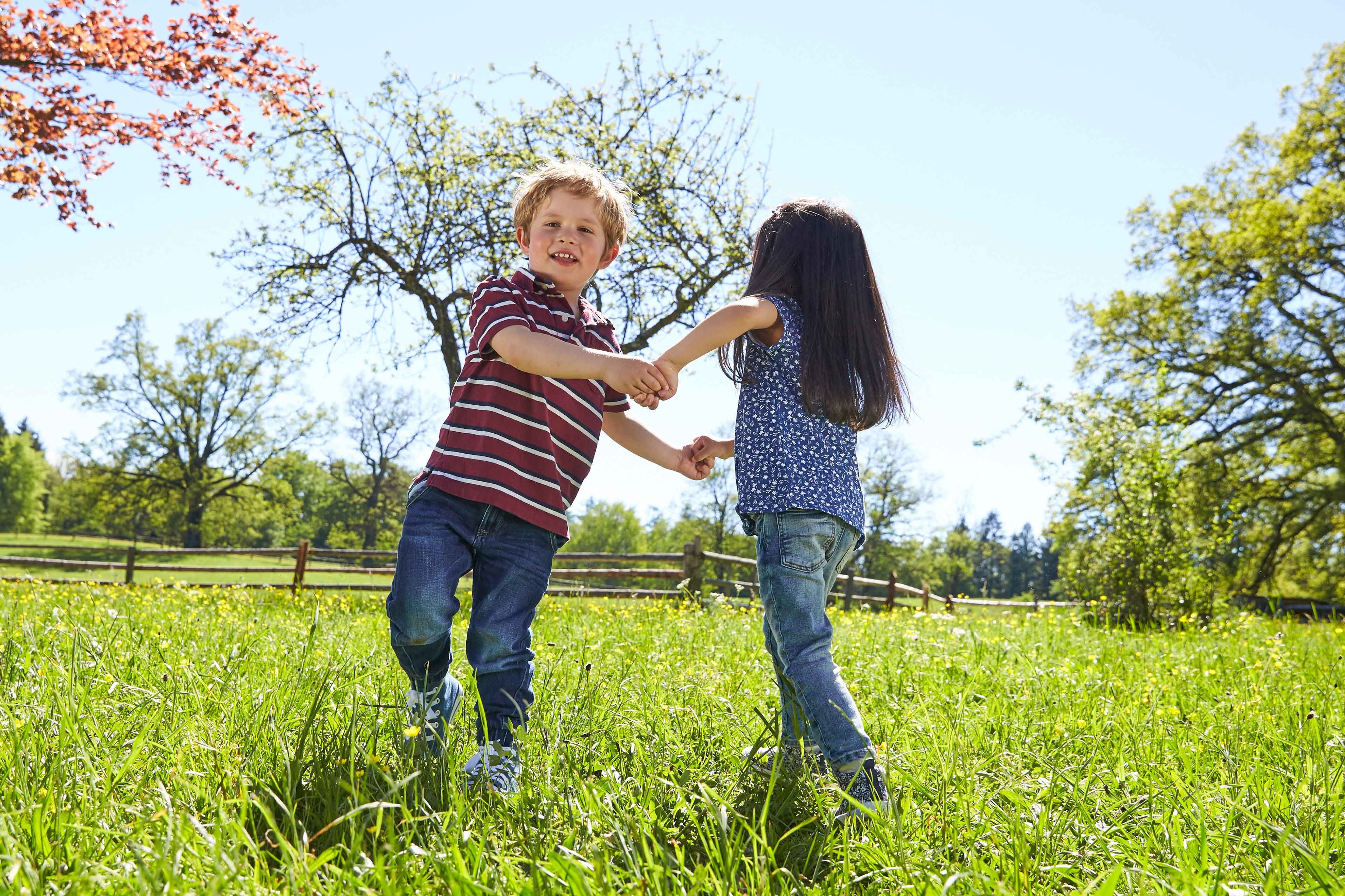 Zwei Kleinkinder halten sich an den Händen und spielen auf einer Wiese im Freien