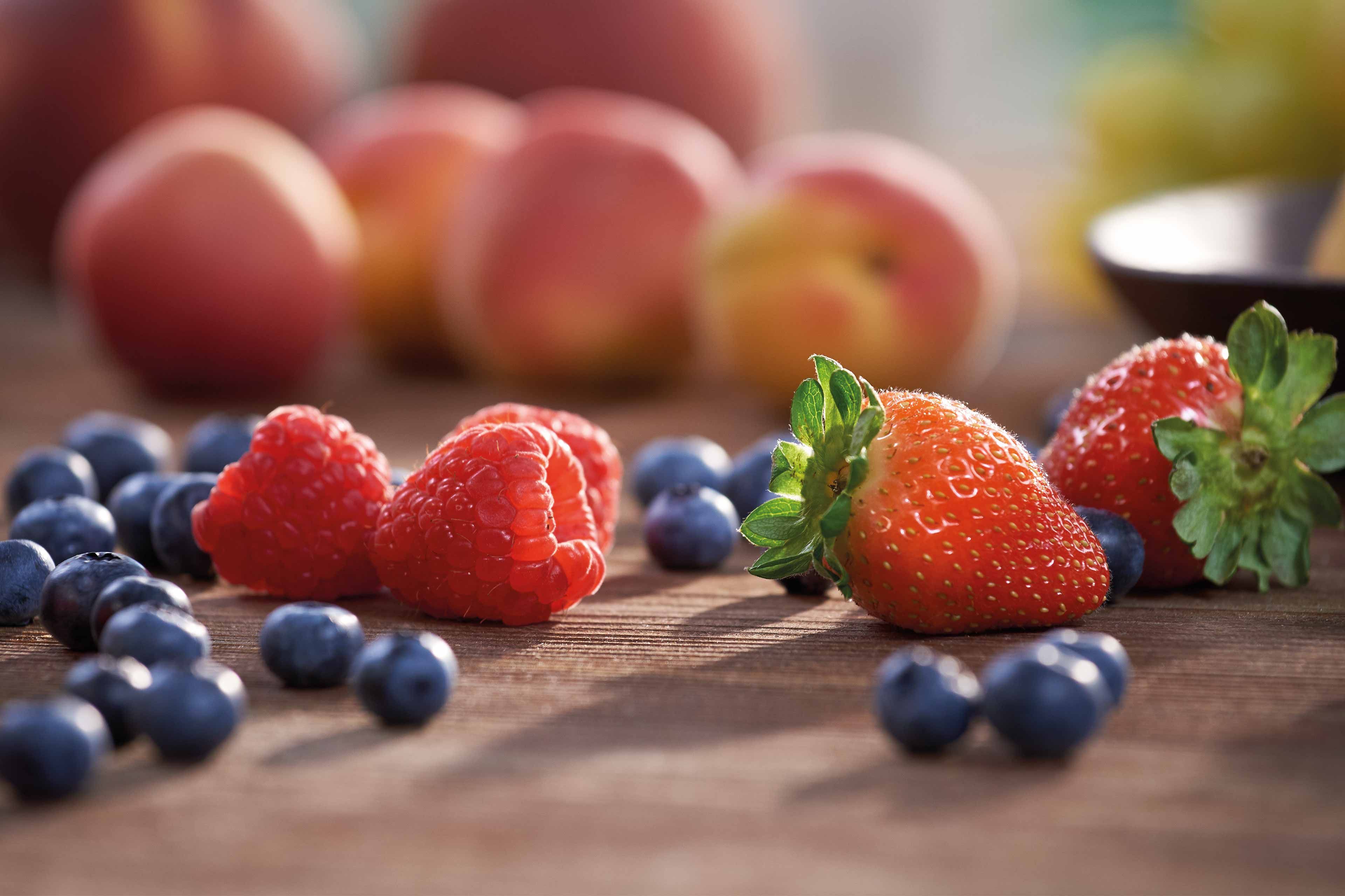 Eine Vielzahl von frischen Früchten, darunter Erdbeeren, Himbeeren und Blaubeeren, auf einer Holzunterlage.