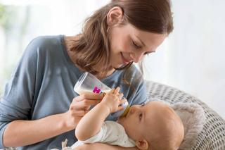 Eine Frau, die ihr Baby mit der Flasche füttert, während beide bequem in einem Raum mit Tageslicht sitzen.