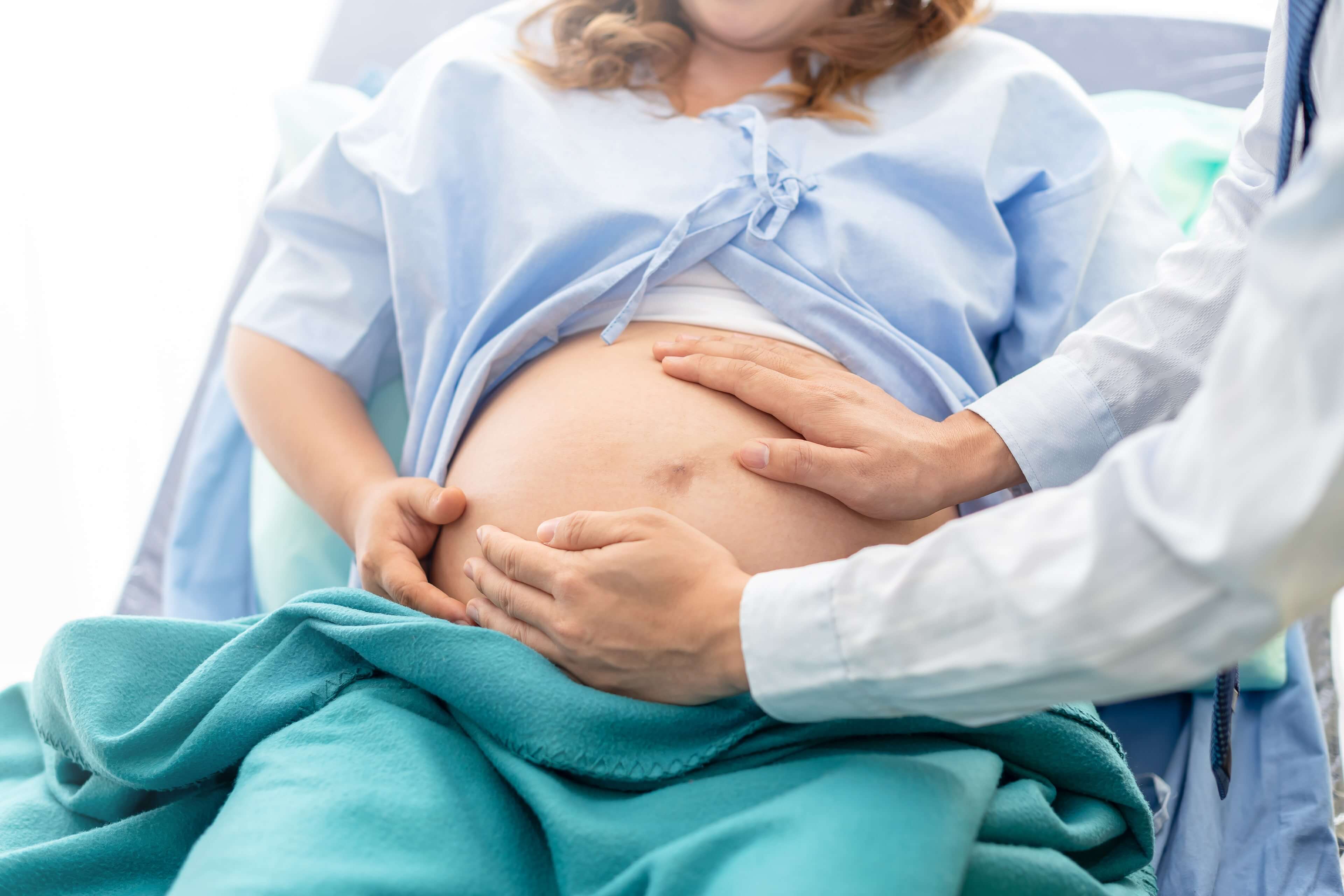 Eine medizinische Fachkraft berührt sanft den Bauch einer schwangeren Frau.