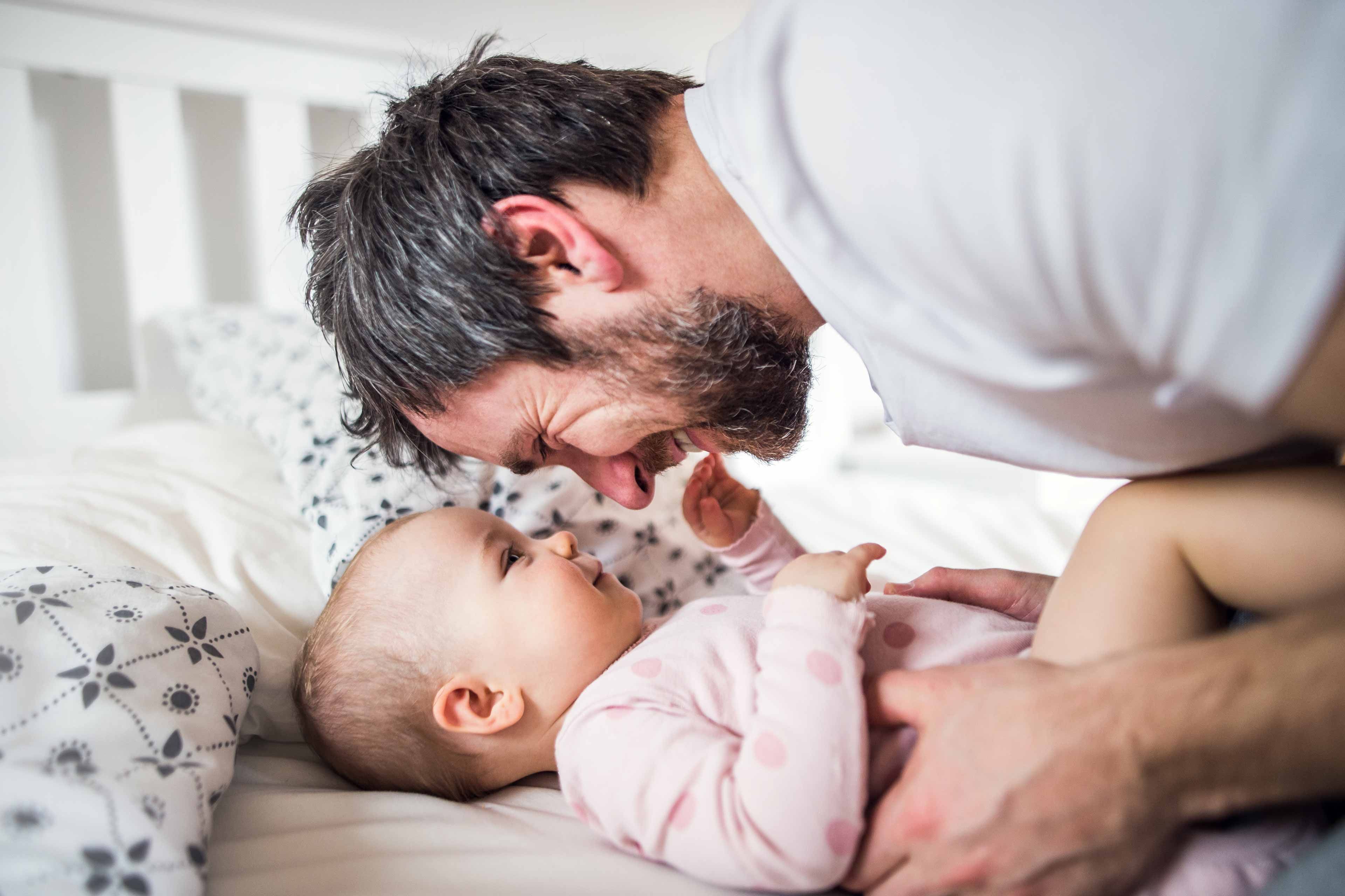 Ein zärtlicher Moment zwischen einem Mann und einem Baby, in dem sich der Mann hinunterbeugt, um das Gesicht des Babys zu berühren, wobei beide eine freudige Interaktion teilen.