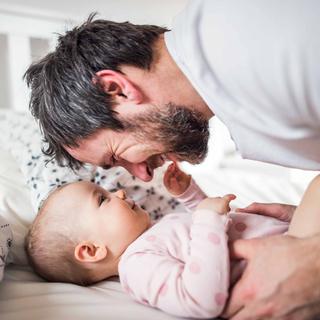 Ein zärtlicher Moment zwischen einem Mann und einem Baby, in dem sich der Mann hinunterbeugt, um das Gesicht des Babys zu berühren, wobei beide eine freudige Interaktion teilen.
