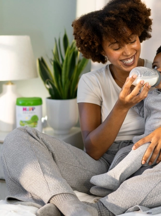 Mum bottle feeding baby in bed