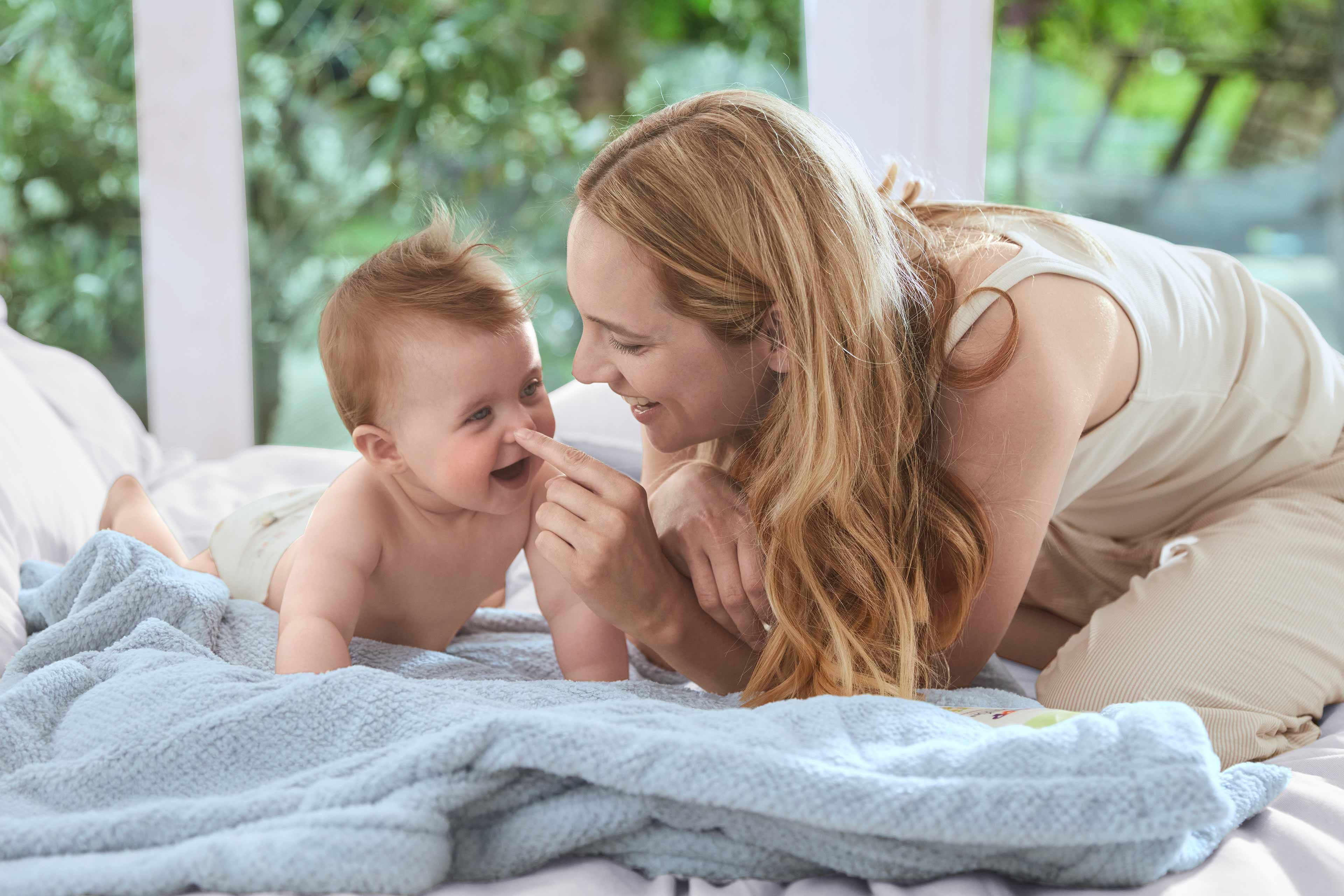 Ein zärtlicher Moment zwischen einer Mutter und ihrem Baby, in dem die Mutter spielerisch das Gesicht des Babys berührt.