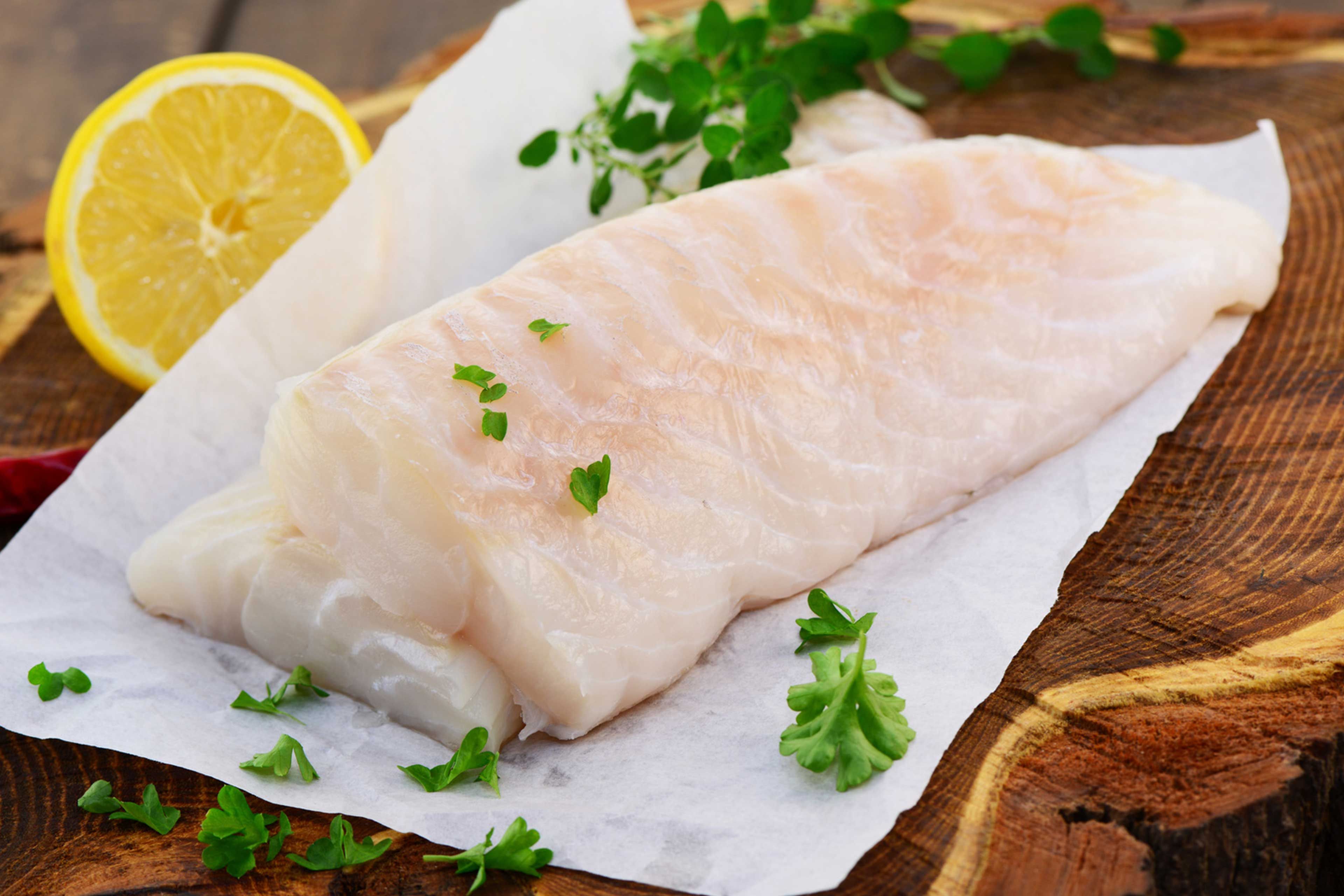 Ein Stück roher Fisch, garniert mit grünen Kräutern und einer Zitronenscheibe.
