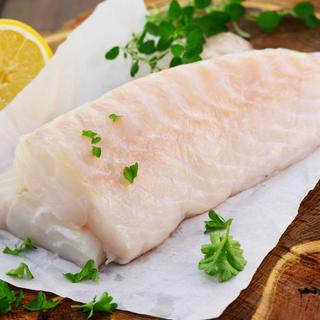 Ein Stück roher Fisch, garniert mit grünen Kräutern und einer Zitronenscheibe.