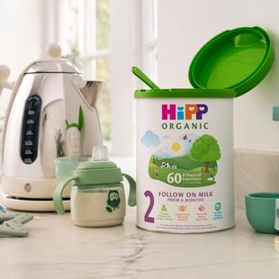 HiPP Organic Follow On Milk powder tin on a bright kitchen worktop beside a baby sippy cup, kettle and baby toys.
